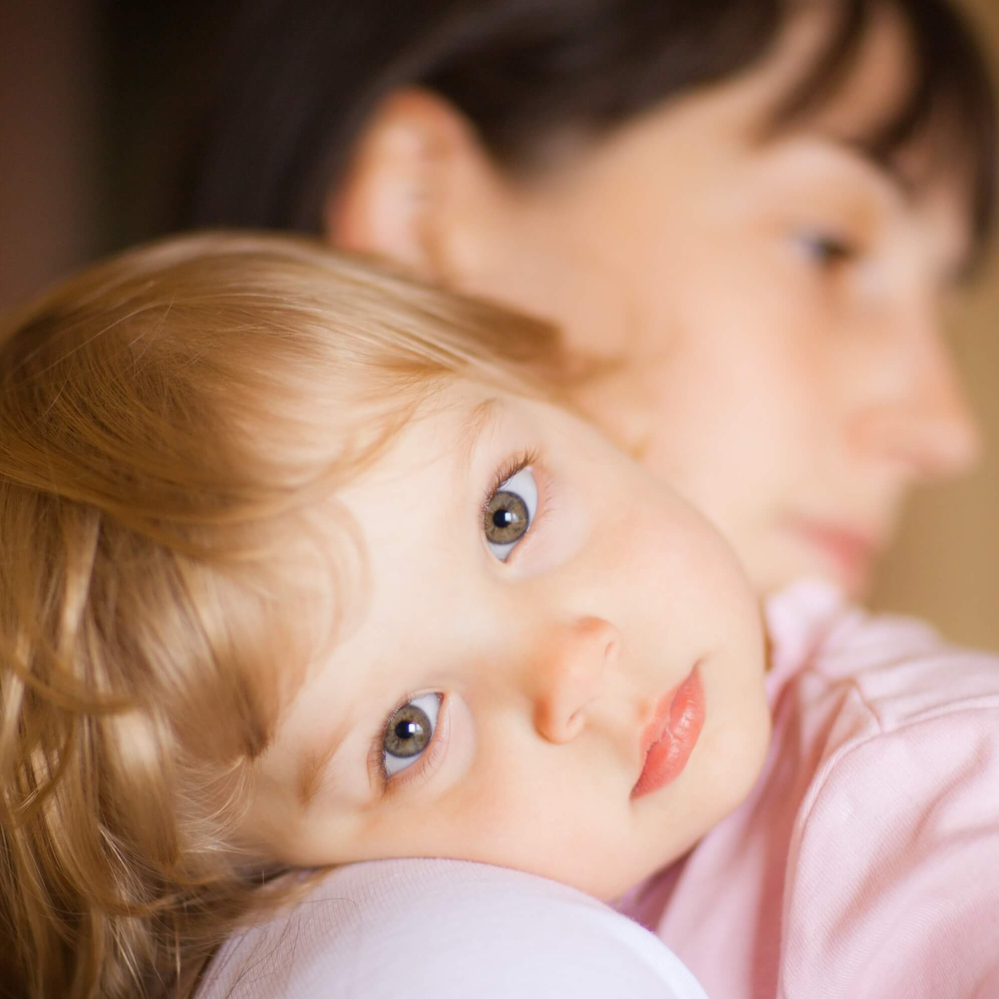 A small childs face as she lays her head on a woman's shoulder