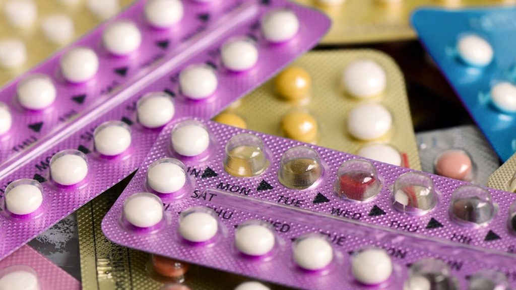 A selection of birth control pills is scattered across the photo, with some pills missing from their packs.