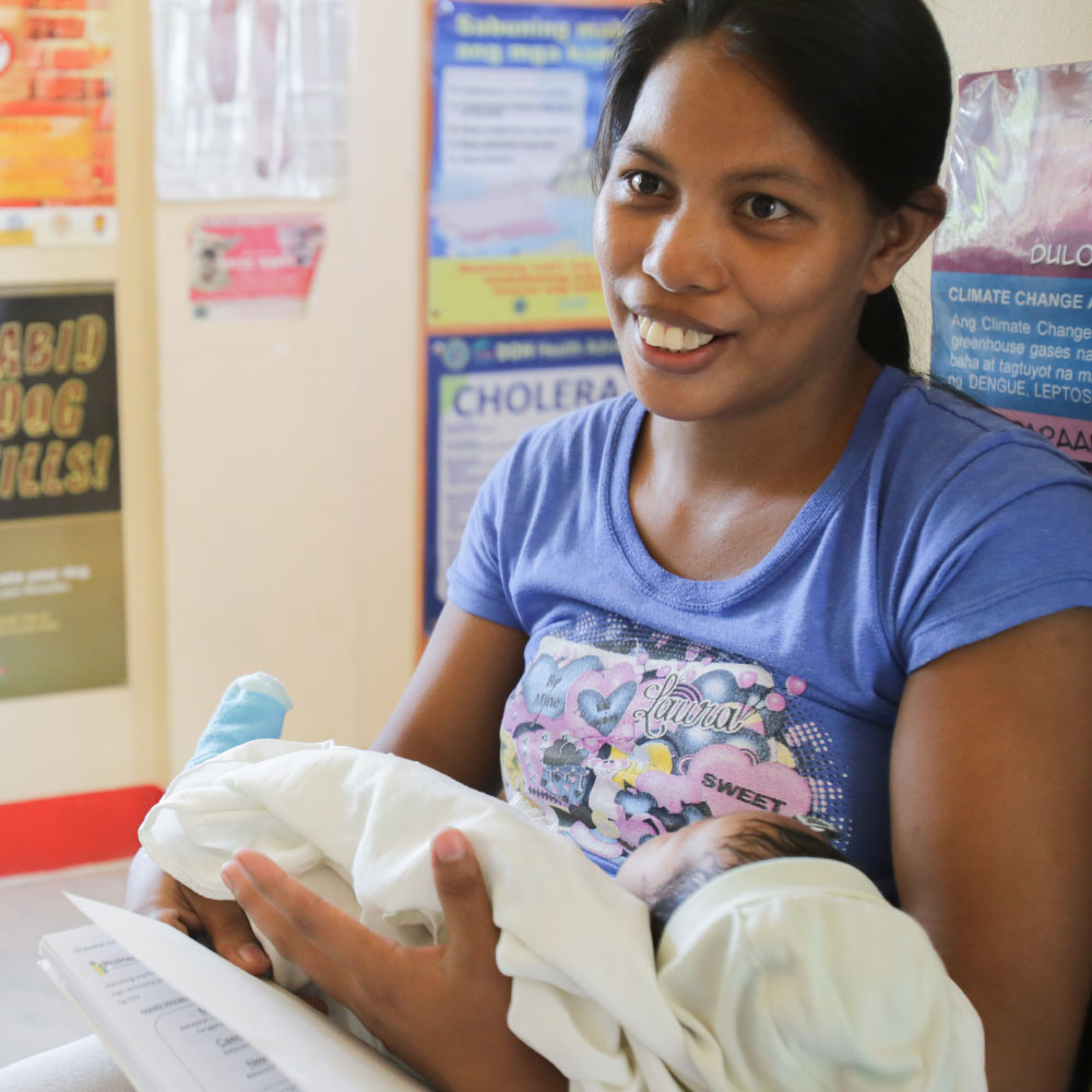 A smiling young mother holds a baby during a medical consultation.