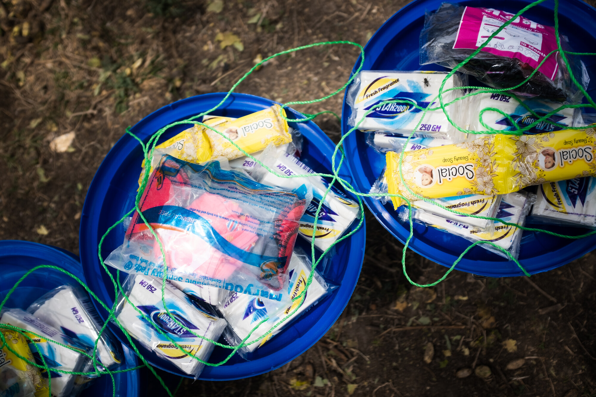 Two blue buckets show items in a dignity kit. Items include sanitary pads, body soap and undergarments.
