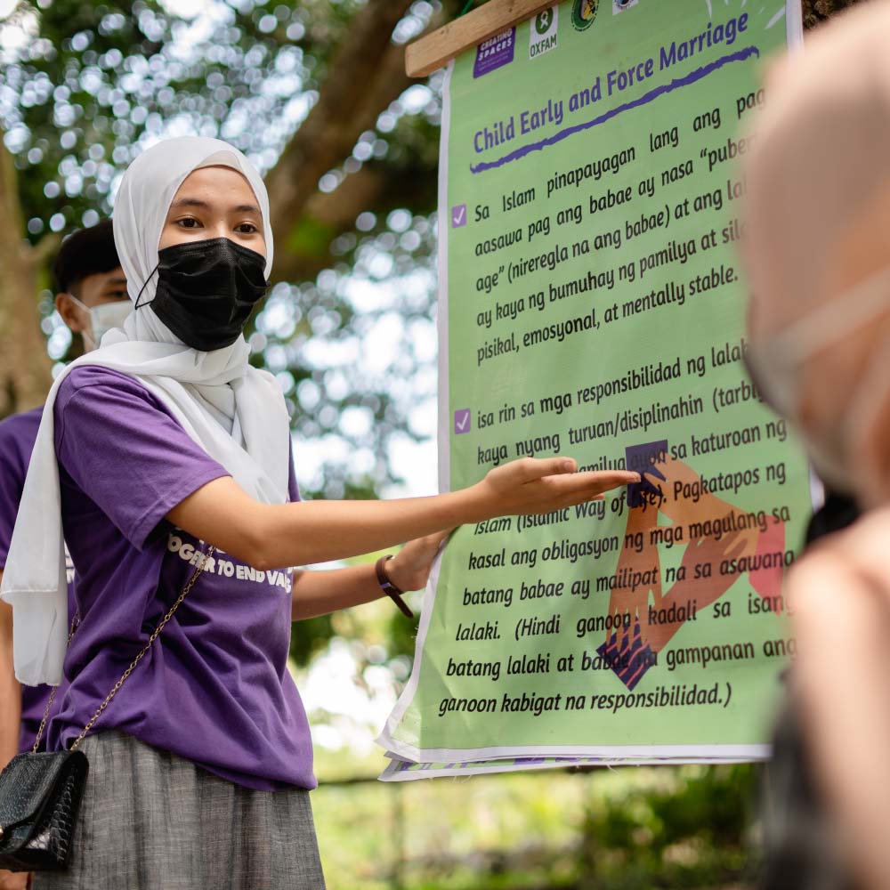 A young woman in the Philippines points to a poster about ending child, early and forced marriage.