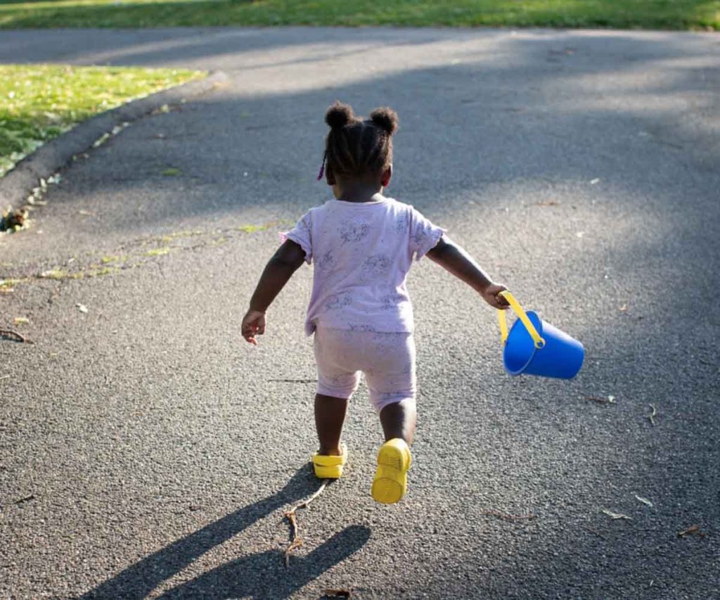 A toddler holding a toy bucket runs outside.