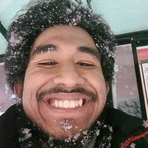 A young person smiling with a moustache and snow on their hair.