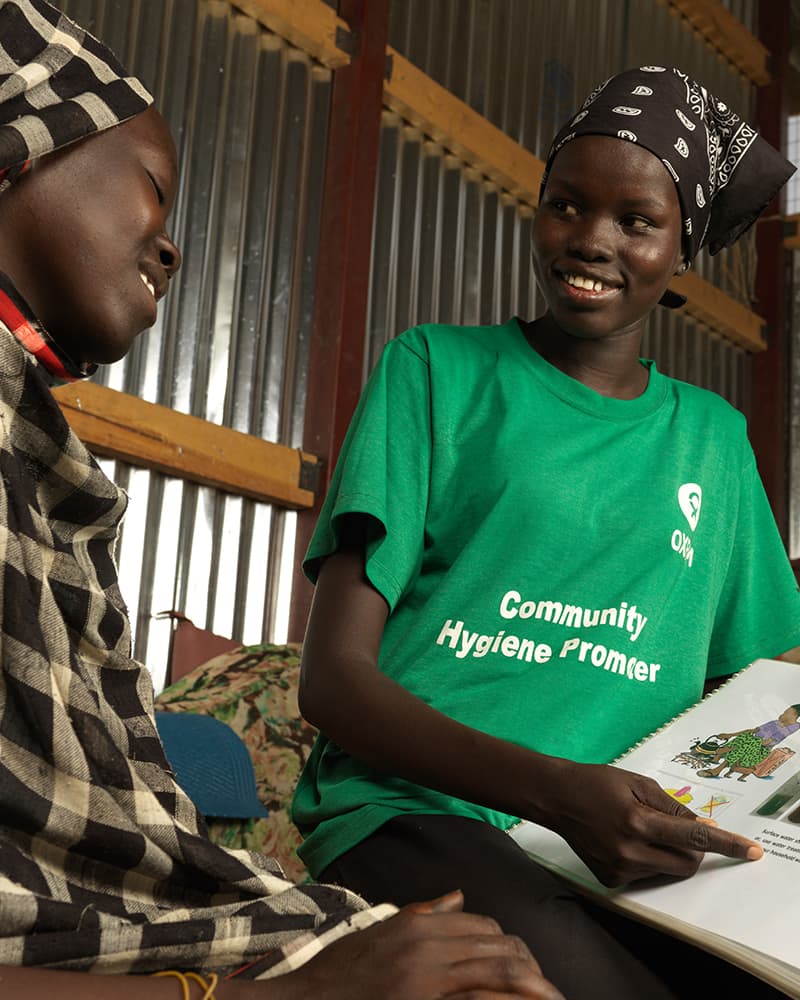 Two women, one an Oxfam community hygiene promoter, are having a conversation about hygiene in a tin shelter.