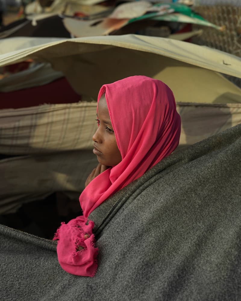 A young girl with a pink headscarf looking out over a sea of tents.