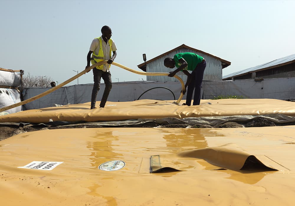 Two men filling a water storage station under the sun in an informal settlement.