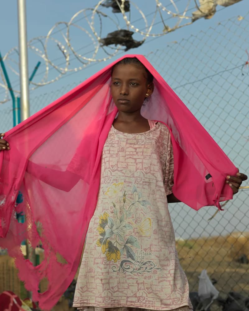 A young girl wearing a pink headscarf and staring away from the camera.