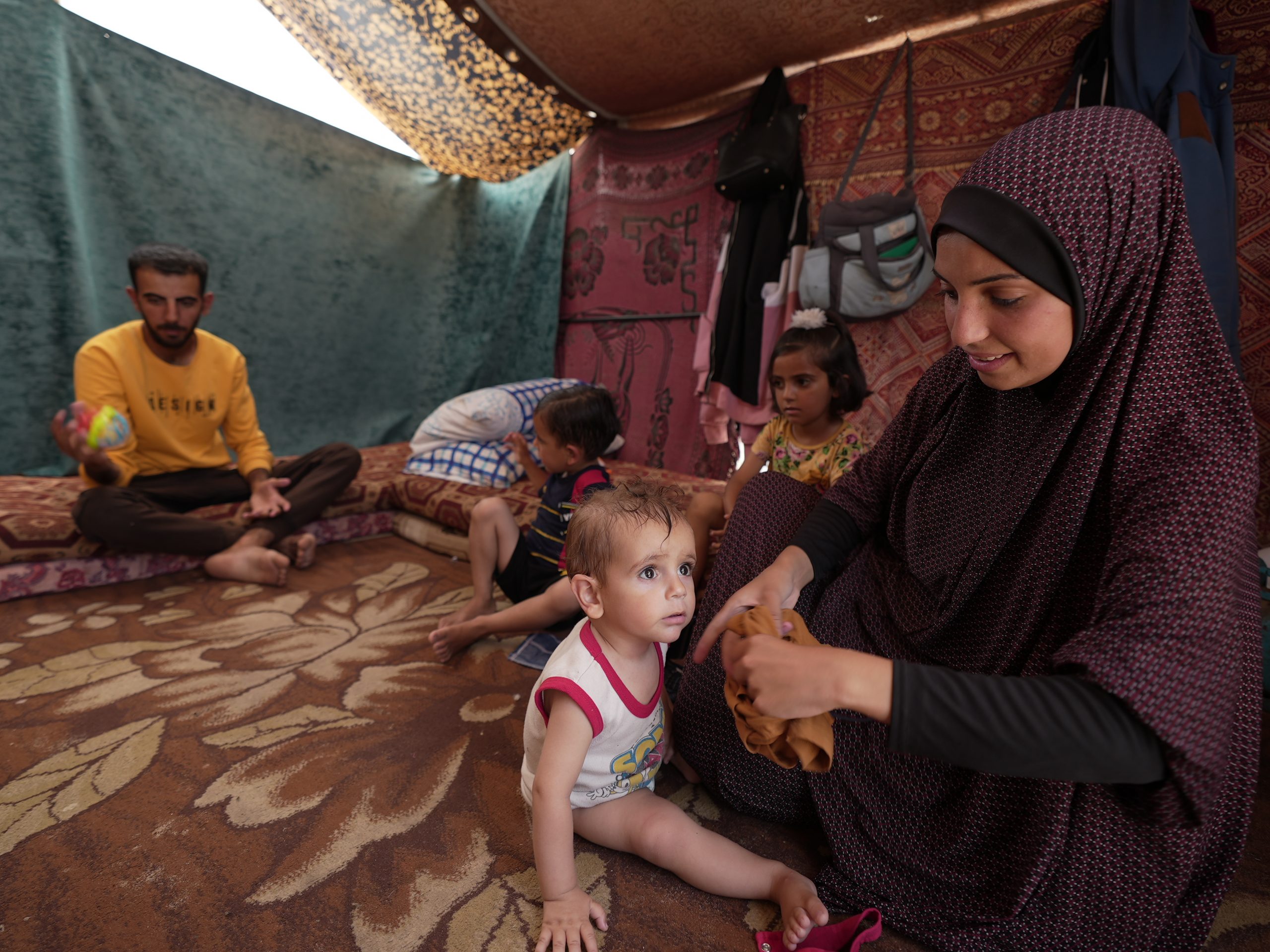 Duaa Abu Sabha is dressing her child in clothes inside her tent in the Al-Mawasi area in Khan Yunis. Photo: Alef Multimedia/Oxfam