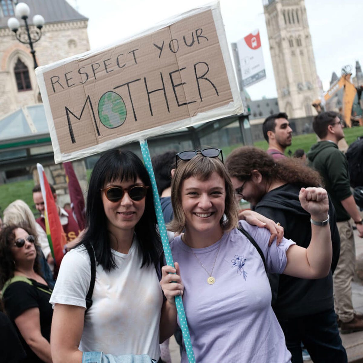 Two women holding a sign: "Respect Your Mother". The O is a circular map of the earth.