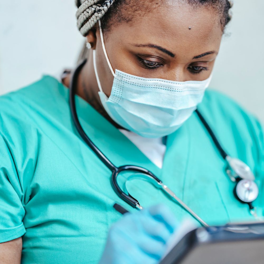 A nurse wearing a face mask writes notes on a medical chart.