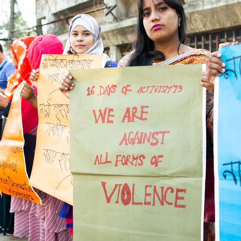 A woman holds a poster that reads ‘We Are Against All Forms of Violence’.