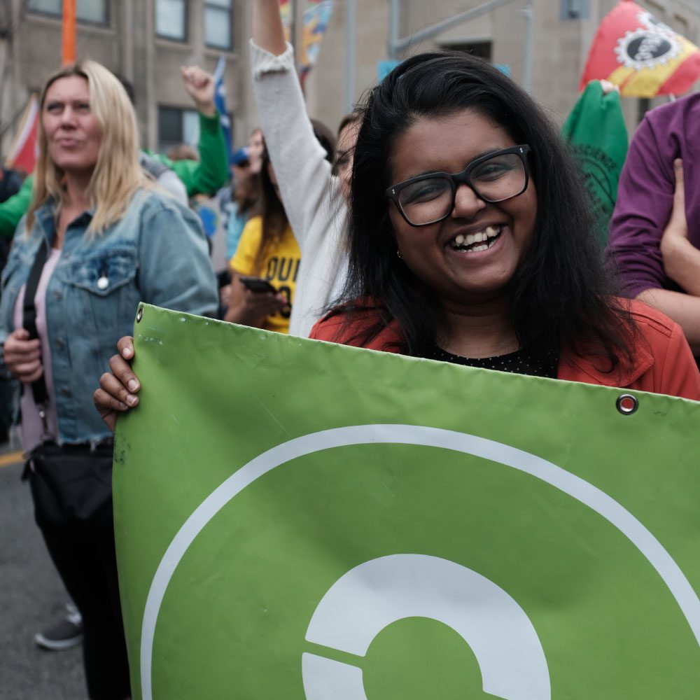 A woman holding an Oxfam Canada banner smiles for the camera.