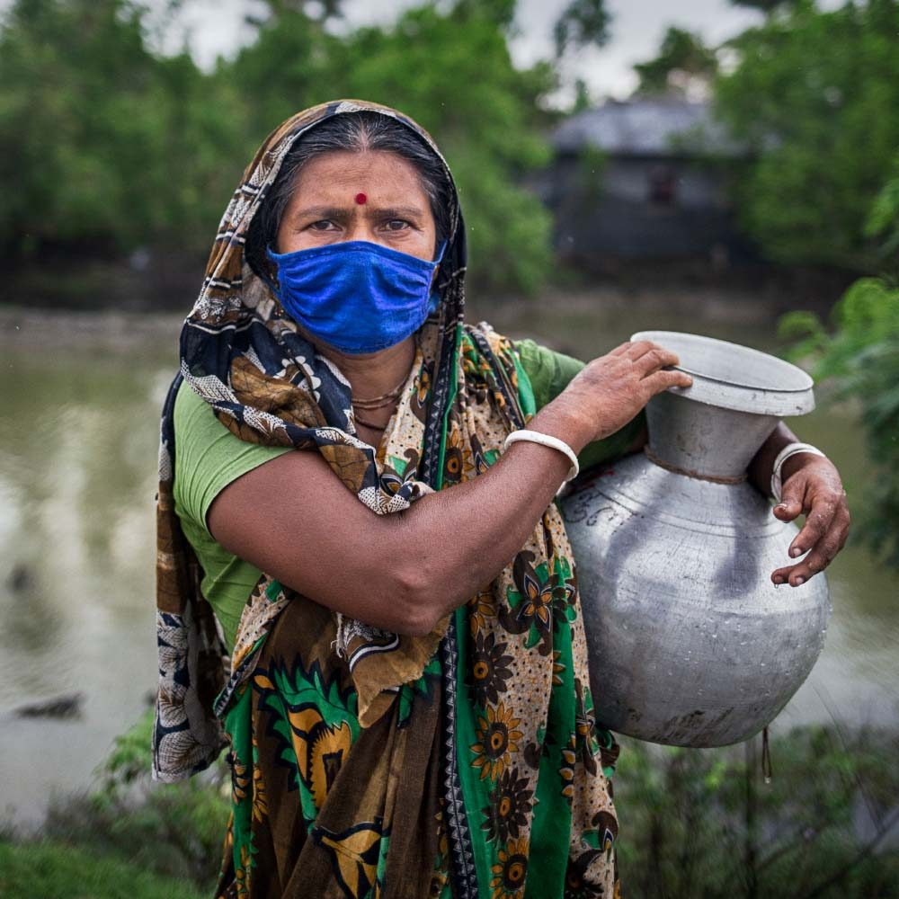 A woman wearing a face mask holds a jug of water.