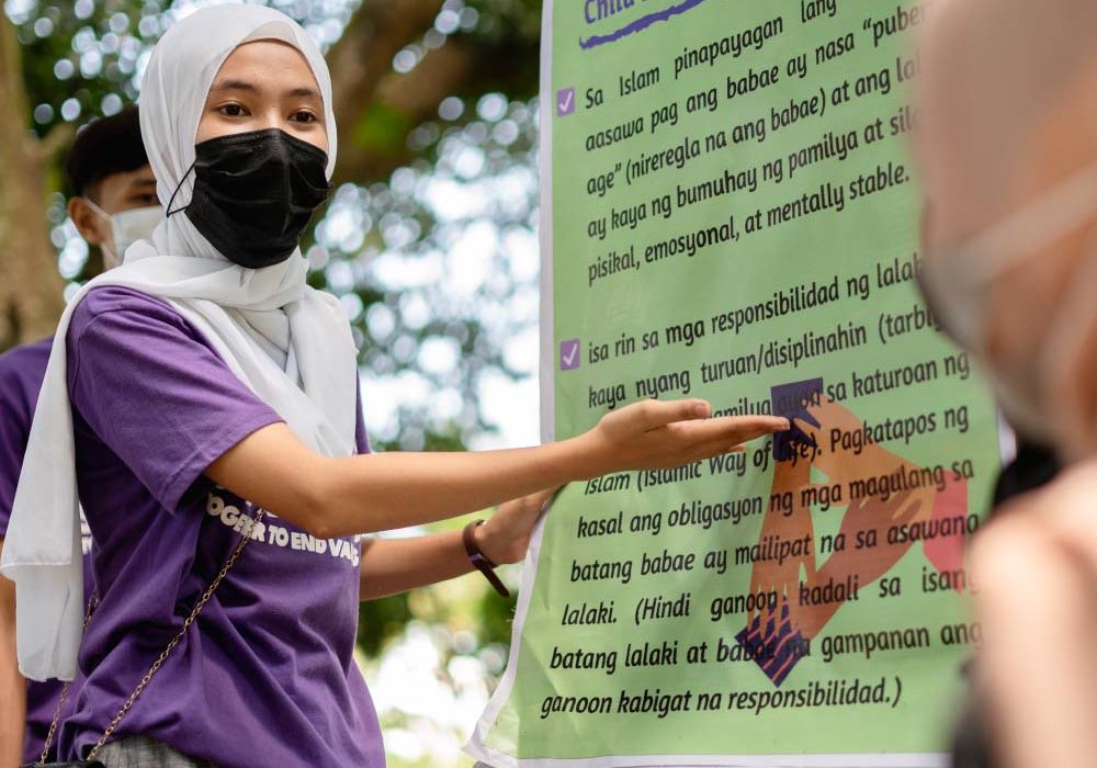 A young woman in the Philippines points to a poster about ending child, early and forced marriage.
