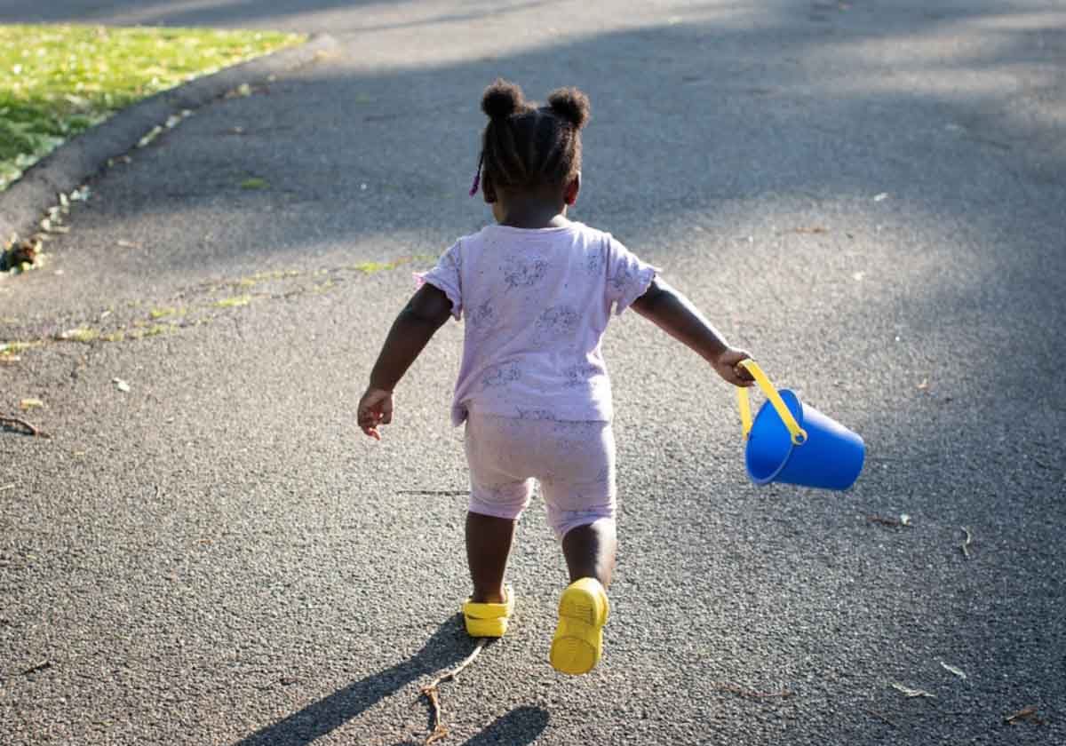 A toddler holding a toy bucket runs outside.