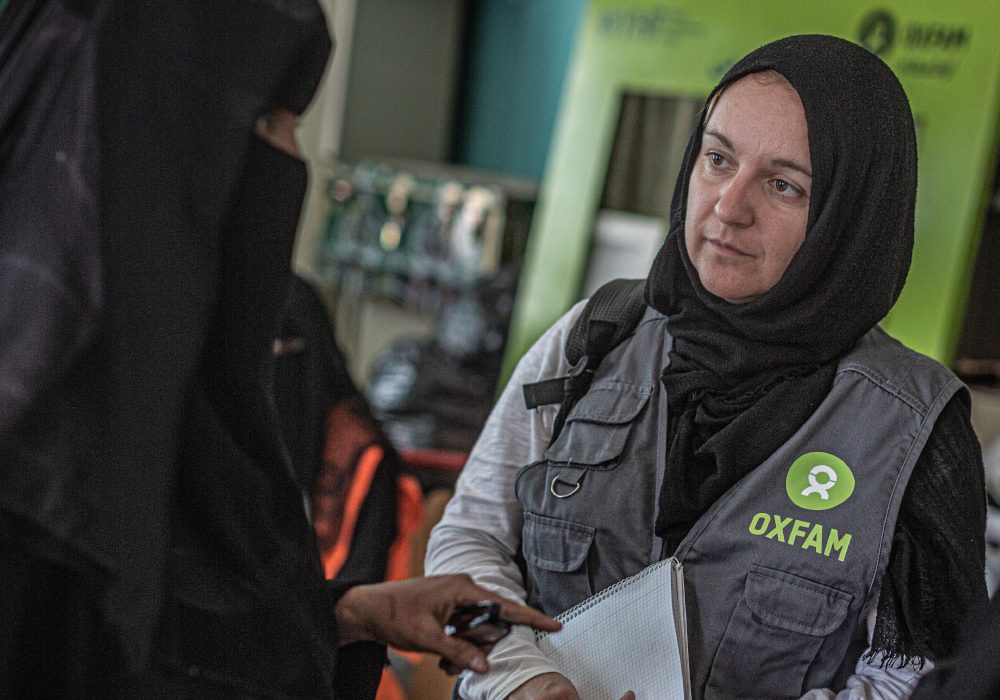 An Oxfam staff member listens to women speaking.