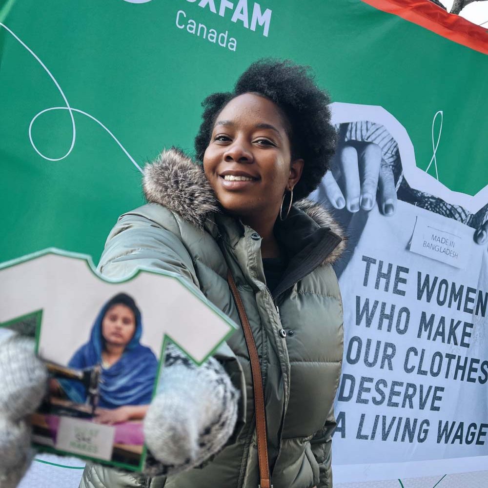 A woman holds an Oxfam branded postcard to the camera.