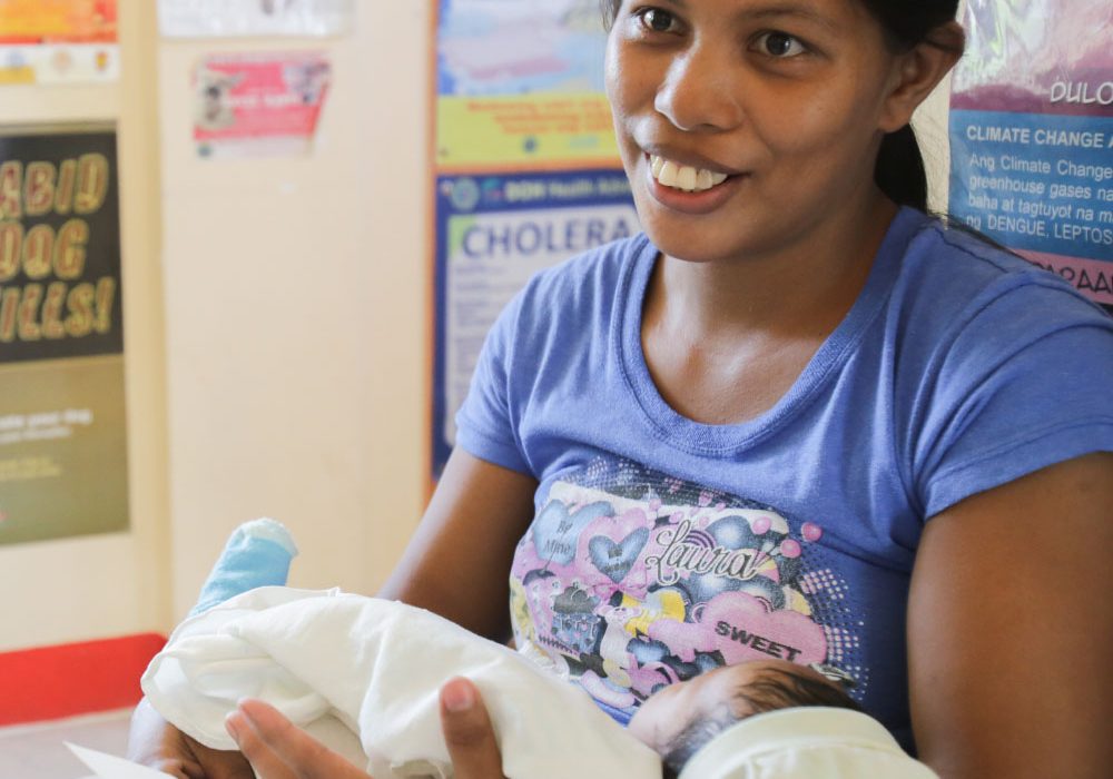 A smiling young mother holds a baby during a medical consultation.