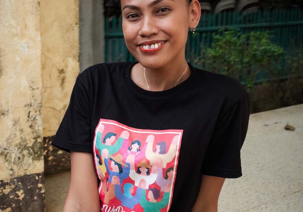 A smiling young woman faces the camera while wearing a shirt that reads ‘We Dare To Lead’.